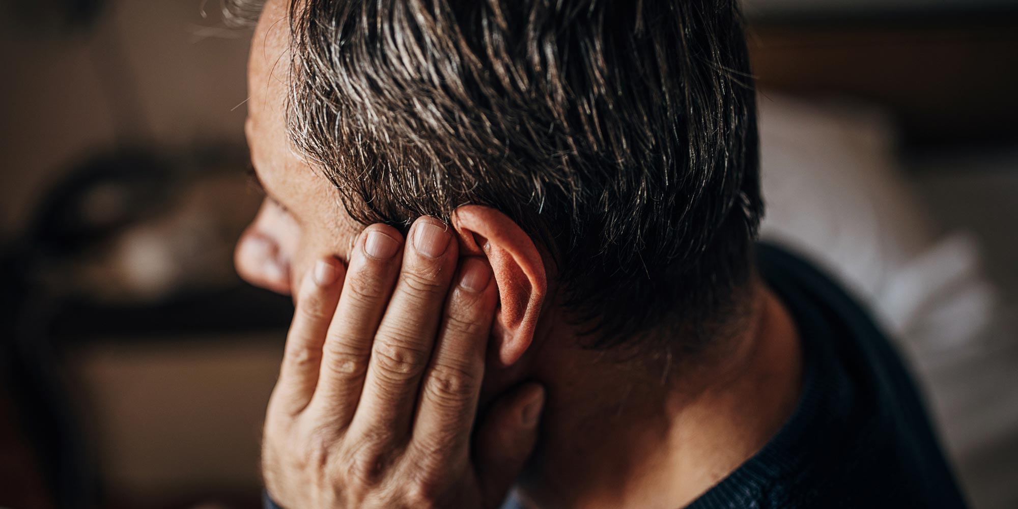 older man holding his ear